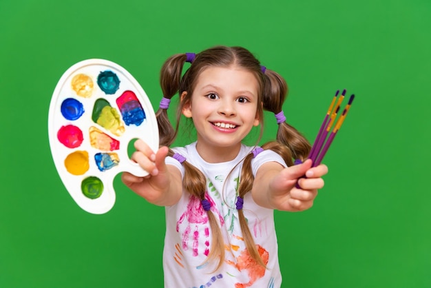 Una niña con pinturas sobre un fondo verde aislado cursos de creatividad para niños en pintura con acuarelas y gouache