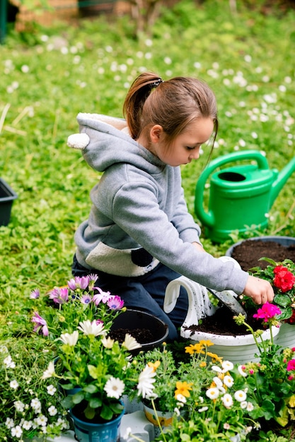 Niña plantando flores con cuidado en una maceta para balcón en el patio trasero.