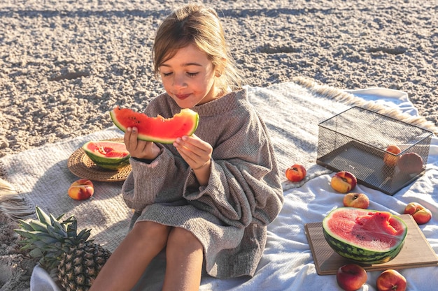 Una niña en una playa de arena come una sandía