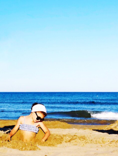 Foto niña en la playa contra el cielo despejado