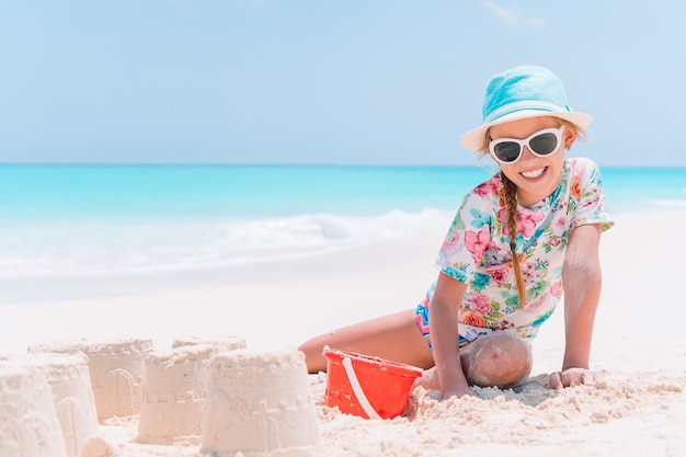 Niña en la playa juega con arena y hace castillos de arena