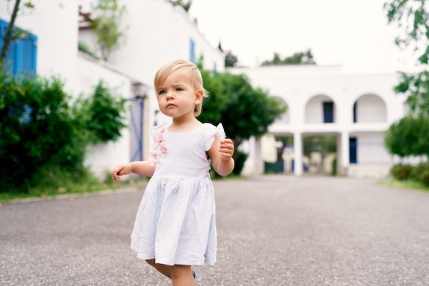 Niña con una pluma en la mano camina por el patio de asfalto