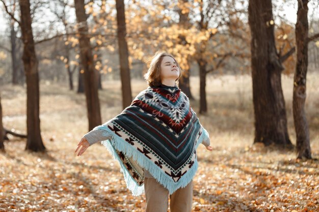 Una niña en un poncho un paseo por el bosque de otoño.