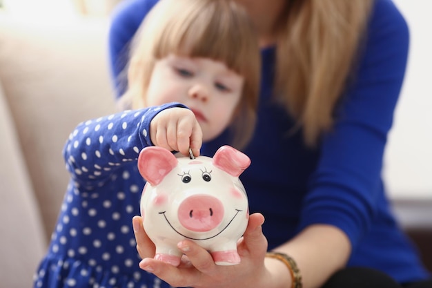 Una niña pone una moneda en una alcancía rosa.