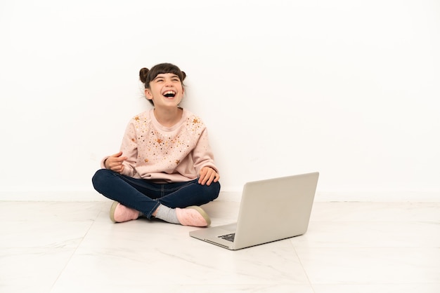 Niña con un portátil sentado en el suelo riendo