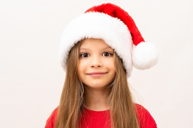 Una niña posando sobre una pared blanca con un sombrero de Navidad.