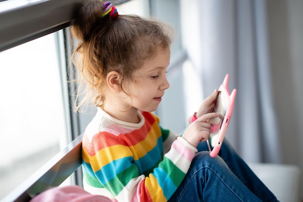 Niña positiva sosteniendo una tableta en sus manos Los niños usan tecnología