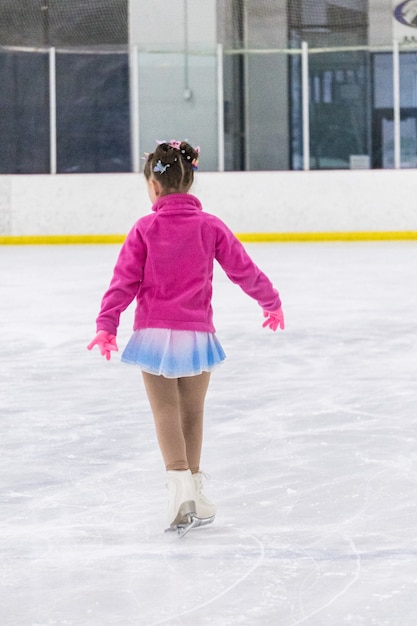 Niña practicando patinaje artístico en una pista de hielo cubierta.