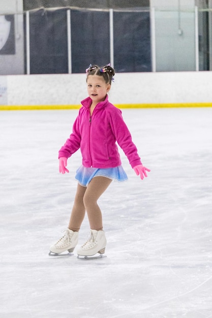 Niña practicando patinaje artístico en una pista de hielo cubierta