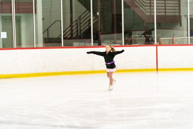 Niña practicando patinaje artístico en una pista de patinaje sobre hielo cubierta.