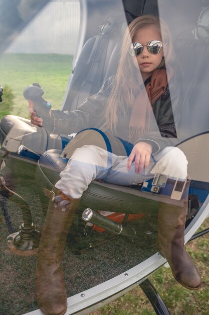 Foto niña preadolescente en el asiento del piloto sosteniendo la manija de control detrás del vidrio de la cabina del helicóptero