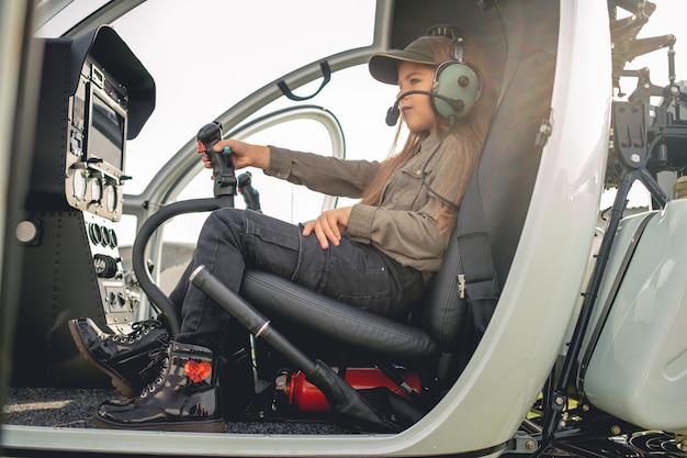 Niña preadolescente centrada en auriculares de aviador sentado en la cabina del helicóptero