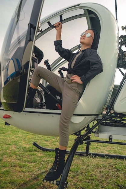 Niña preadolescente en gafas de sol espejadas mirando hacia el cielo desde los escalones del helicóptero