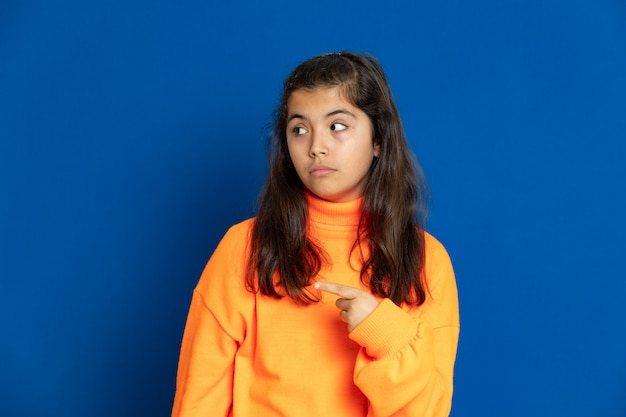 Niña preadolescente con jersey amarillo gesticulando sobre pared azul