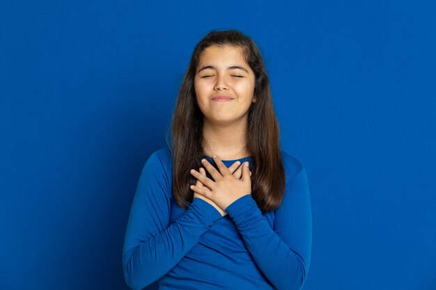 Niña preadolescente con jersey azul gesticulando sobre pared azul