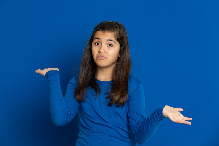 Foto niña preadolescente con jersey azul gesticulando sobre pared azul
