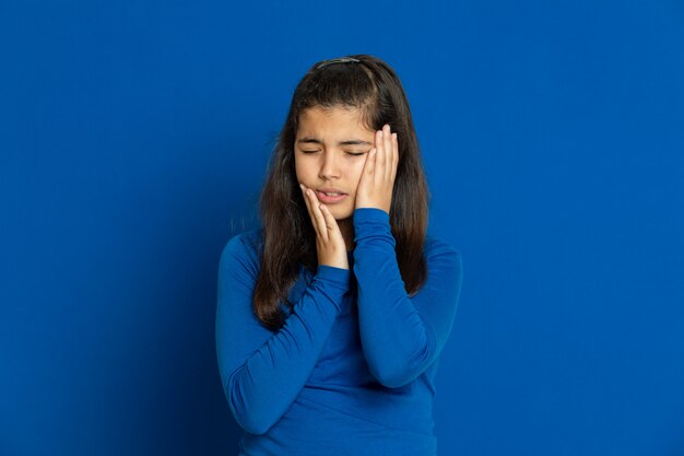 Niña preadolescente con jersey azul gesticulando sobre pared azul