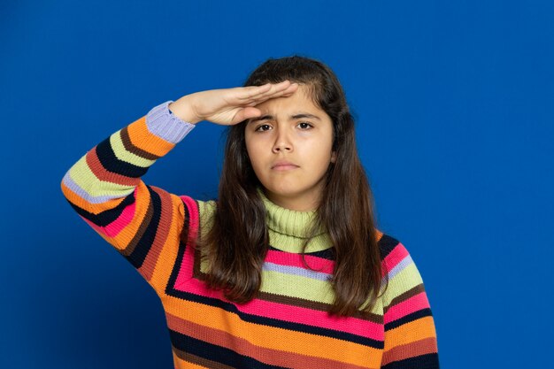 Niña preadolescente con jersey a rayas gesticulando sobre la pared azul