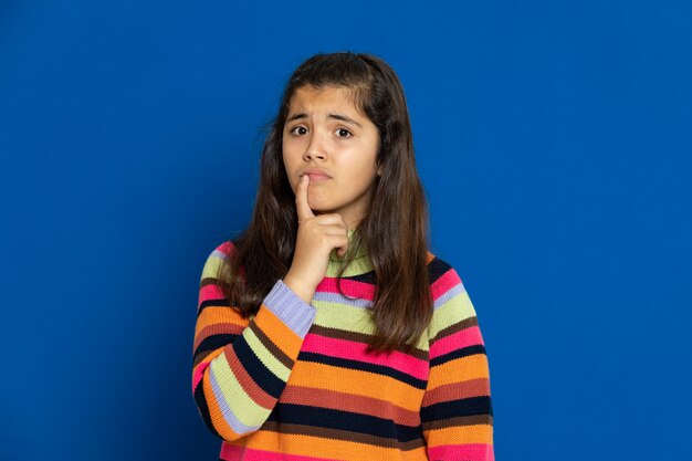 Niña preadolescente con jersey a rayas gesticulando sobre la pared azul