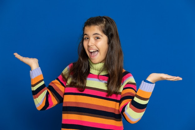 Niña preadolescente con jersey a rayas gesticulando sobre la pared azul