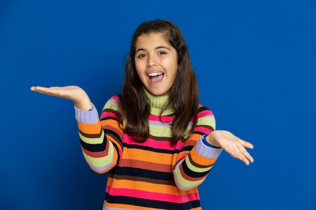 Niña preadolescente con jersey a rayas gesticulando sobre la pared azul