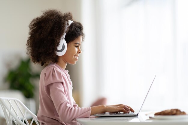 Niña preadolescente negra feliz que usa una computadora portátil para hacer la tarea