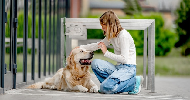 Niña preadolescente con perro golden retriever sentado en la ciudad en la calle