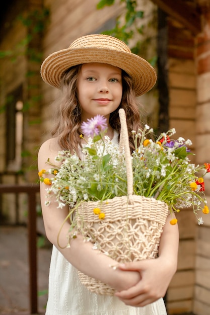 Niña preadolescente sonriente sosteniendo una cesta de mimbre con coloridas flores silvestres en el día de verano