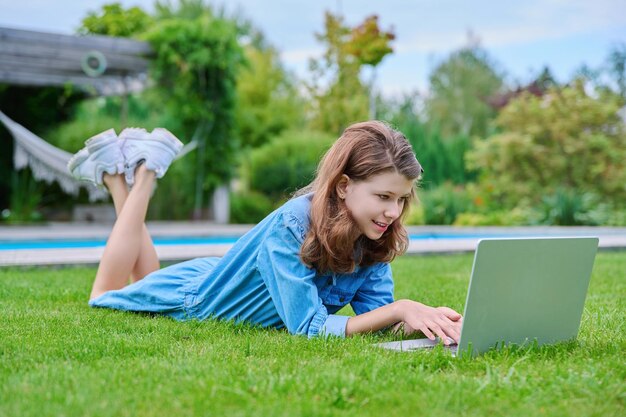 Niña preadolescente tumbada en el césped en el patio trasero usando una computadora portátil para relajarse y estudiar