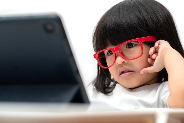 Niña preescolar asiática con gafas rojas y usando tablet pc con fondo blanco