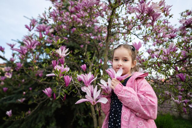 Niña preescolar con chaqueta rosa disfrutando de un agradable día de primavera cerca del árbol floreciente de magnolia Actividades de primavera