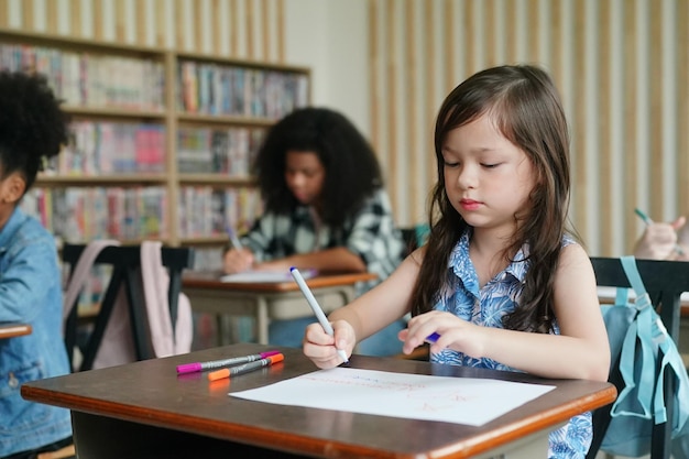 Niña preescolar Kid dibujo con lápiz de color sobre papel blanco sobre la mesa en el aula con amigos