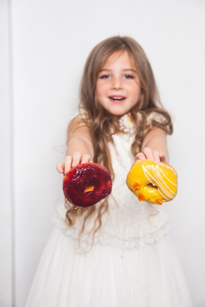 Niña preescolar linda feliz está comiendo donuts coloridos sobre fondo blanco aislado.