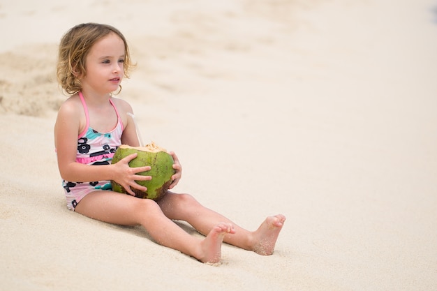 Niña preescolar niño bebiendo jugo de coco en la playa del océano.