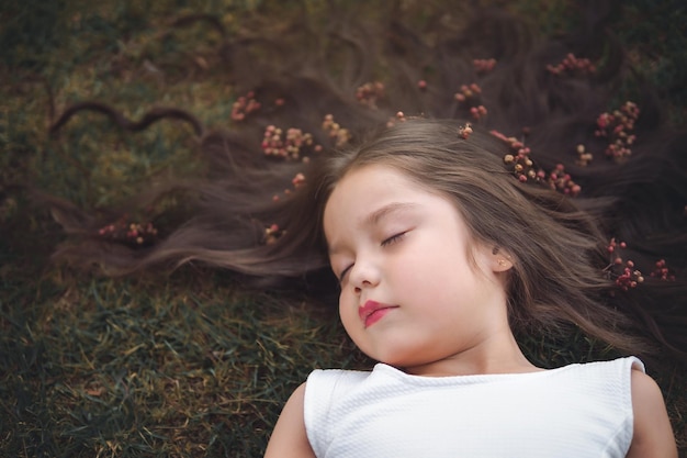 Niña preescolar rubia de pelo largo tirada en la hierba tema del día de los niños