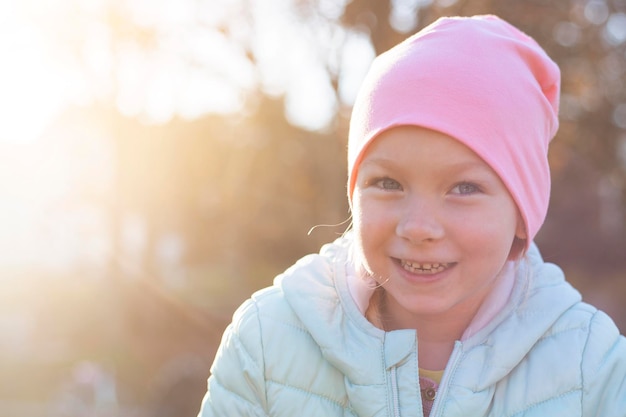 Niña preescolar sonriente con una chaqueta en un sombrero rosa en un día soleado