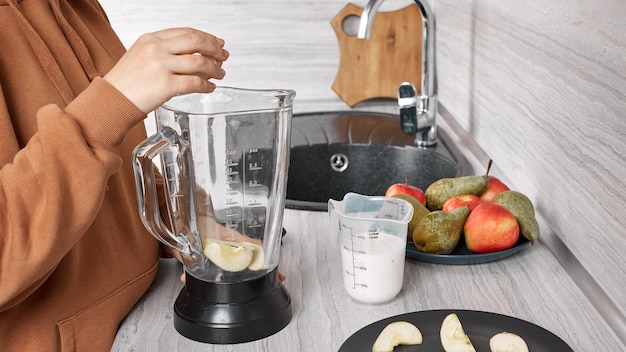 Una niña prepara un batido de manzanas en una licuadora.