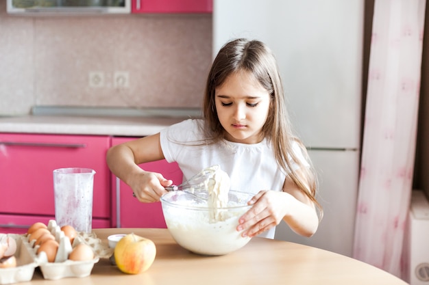 Niña prepara el desayuno, hornea, revuelve en un tazón de harina, leche, huevos, panqueques, los niños ayudan a la madre, desayuno familiar, cocina