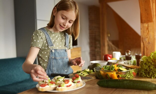 Niña preparando sándwiches con tomates de aguacate, cerezas y verduras en las bruschetas vegetarianas de la cocina