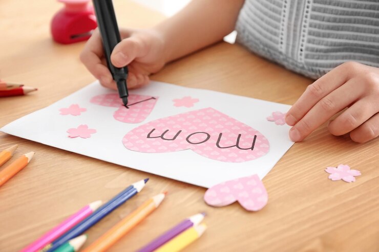 Foto niña preparando la tarjeta de felicitación para su mamá en el día de la madre en la mesa
