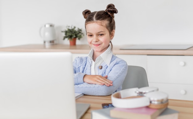 Foto niña prestando atención a su maestra en una clase en línea