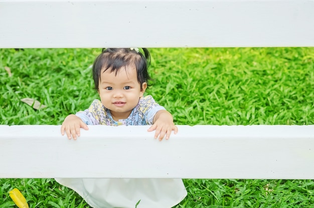 La niña del primer coge una cerca blanca en piso de la hierba en el fondo del jardín con la cara de la sonrisa