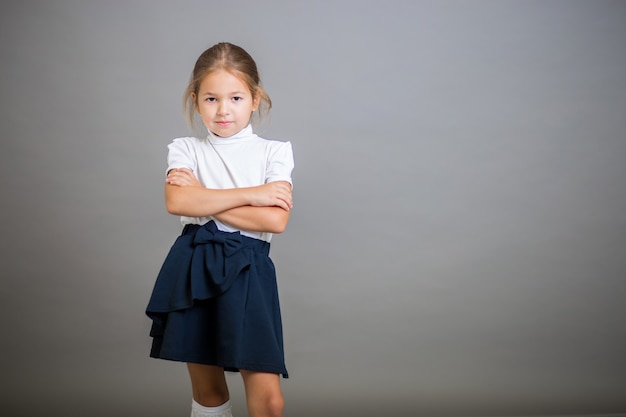 La niña de primer grado con uniforme escolar: una falda y una blusa blanca posa en gris (NO ESCRIBA "THE" IN THE TAGS ")