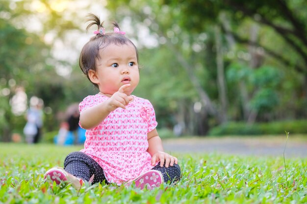 La niña del primer se sienta en el piso de la hierba en el parque con el fondo ligero del sol en el movimiento lindo
