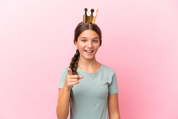 Niña princesa caucásica aislada de fondo rosa sorprendida y apuntando al frente