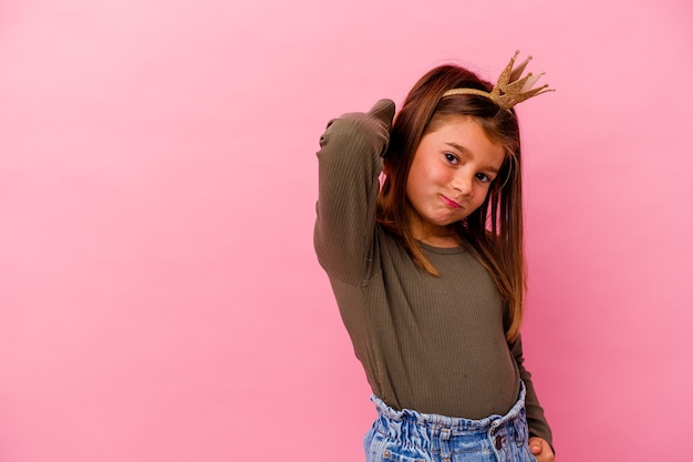 Niña princesa con corona aislada sobre fondo rosa tocando la parte posterior de la cabeza, pensando y haciendo una elección.