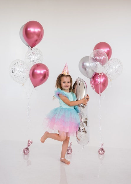 Niña princesa se encuentra con globos sobre un fondo blanco con un lugar para el texto. Celebración de cumpleaños