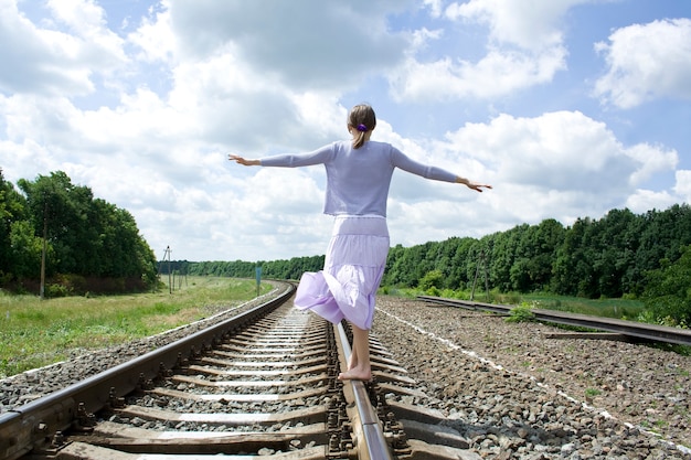 Una niña que camina en el ferrocarril bajo el cielo azul.