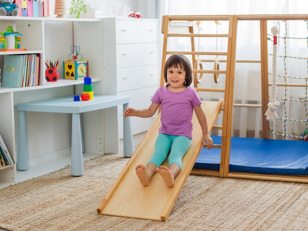 Niña que se divierte montando una montaña rusa en una escalera de complejo de juegos deportivos de casa de madera