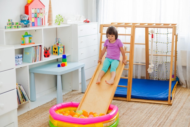 Niña que se divierte montando una montaña rusa en una escalera de complejo de juegos deportivos de casa de madera